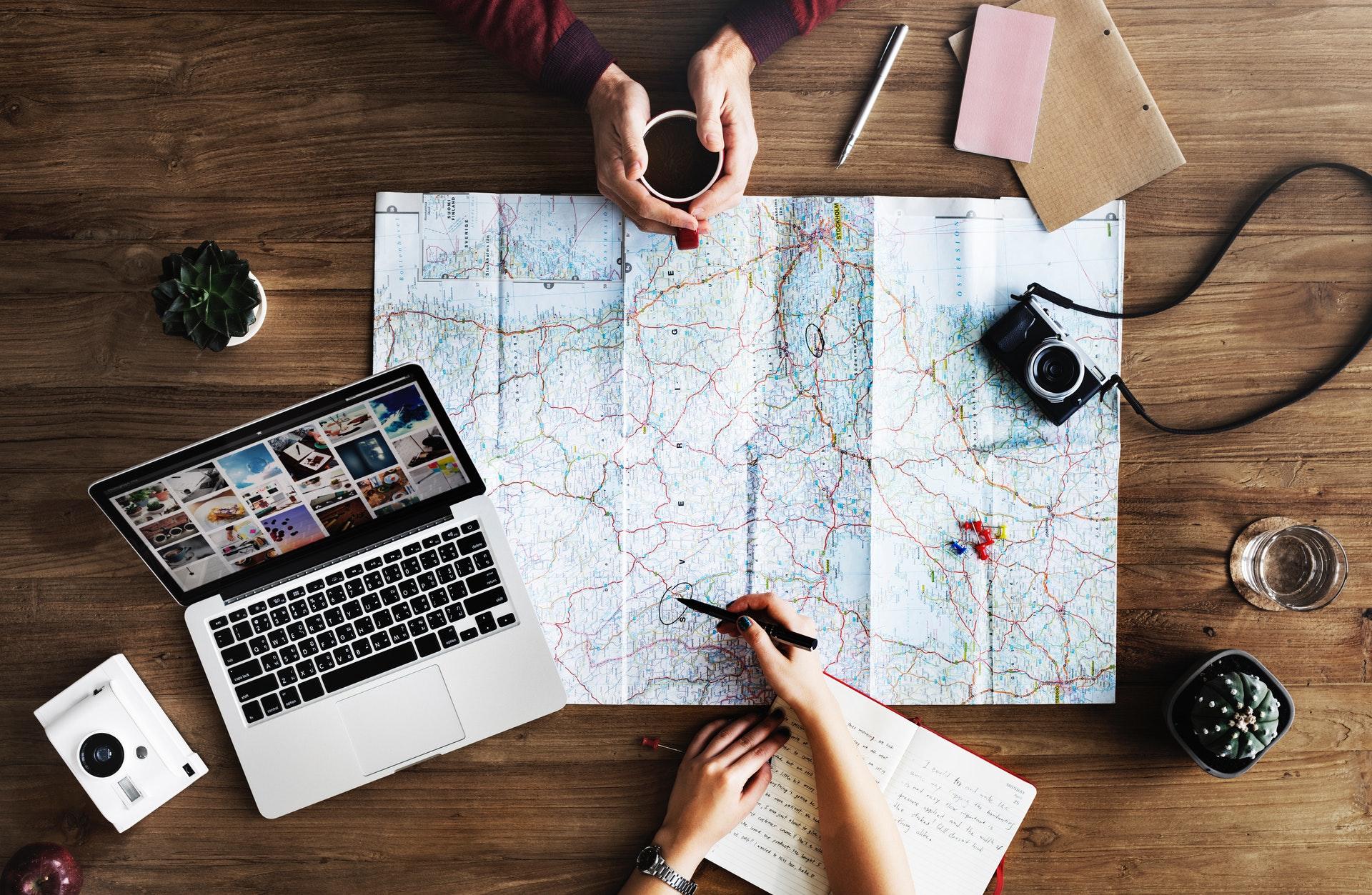 Two people trip planning with laptop, cameras and map